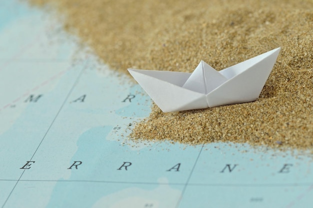 Bateau en papier sur une carte avec du sable - concept d'immigration