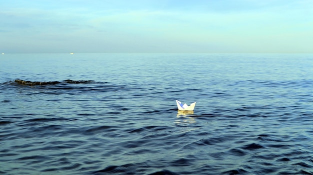 Le bateau en papier flotte dans l'eau bleue de la mer, le symbole du voilier de l'expédition, le concept de voyage, la voile