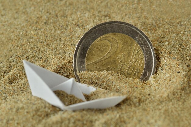 Photo bateau en papier et pièce sur sable