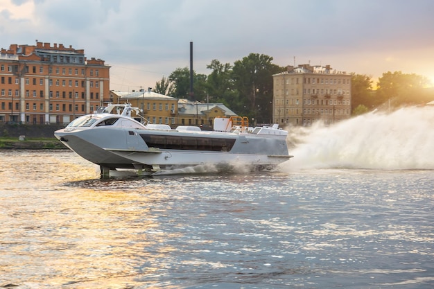 Un bateau à passagers à grande vitesse navigue sur la rivière avec des éclaboussures au coucher du soleil