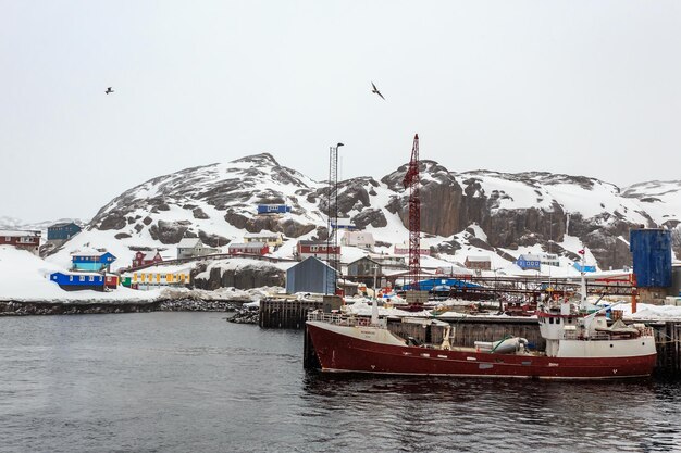 Bateau de pêche à l'embarcadère du village de Maniitsoq avec des maisons colorées sur les rochers en arrière-plan Groenland