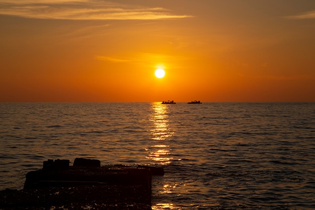Bateau de pêche à l'horizon, coucher de soleil sur la mer. Mer calme, ciel de corail, pêche en soirée