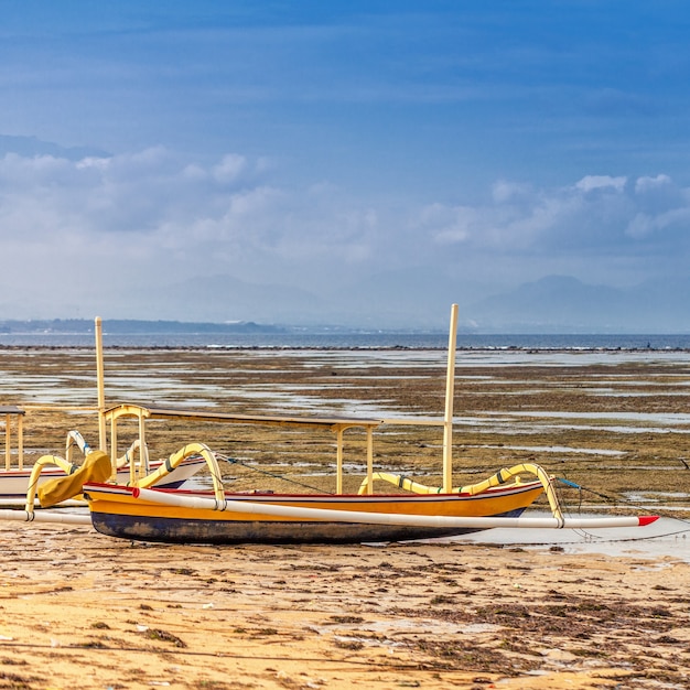 Bateau de pêche traditionnel balinais se dresse sur le rivage de l'océan et la côte à marée basse.