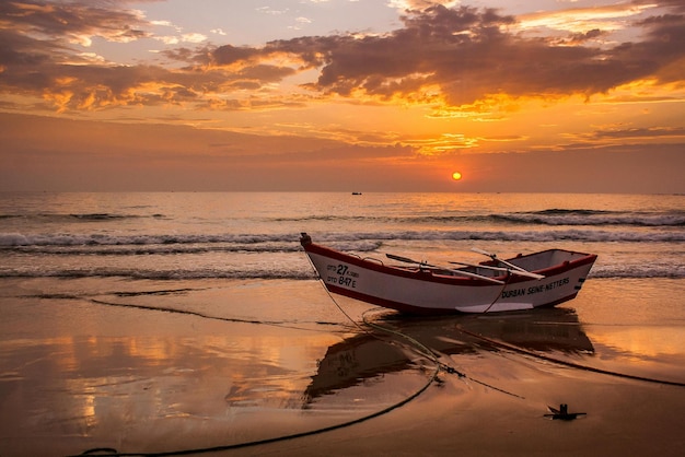 Photo un bateau sur la plage avec le soleil qui se couche derrière lui