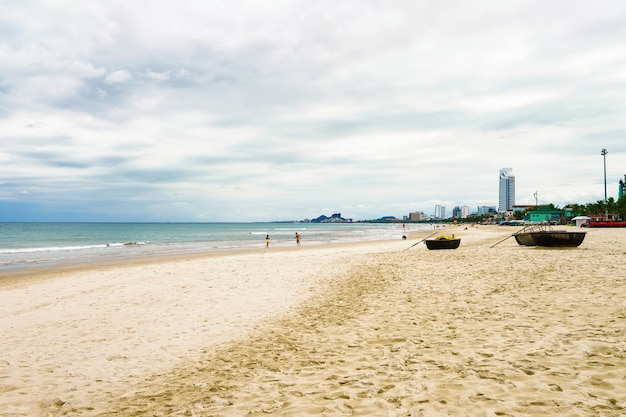 Bateaux de palmiers et touristes à la China Beach à Danang au Vietnam. Elle est aussi appelée plage de Non Nuoc. Mer de Chine méridionale et montagnes de marbre en arrière-plan.