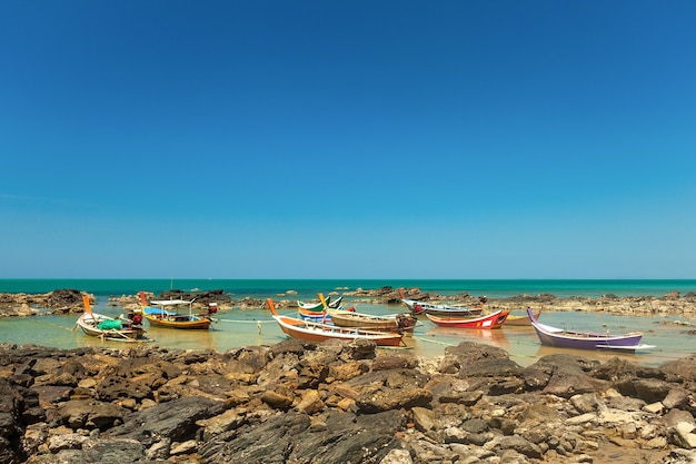 Photo les bateaux de pêche de style thaïlandais en bois colorés se tiennent près de la côte rocheuse dans le contexte de la mer et du ciel bleu.