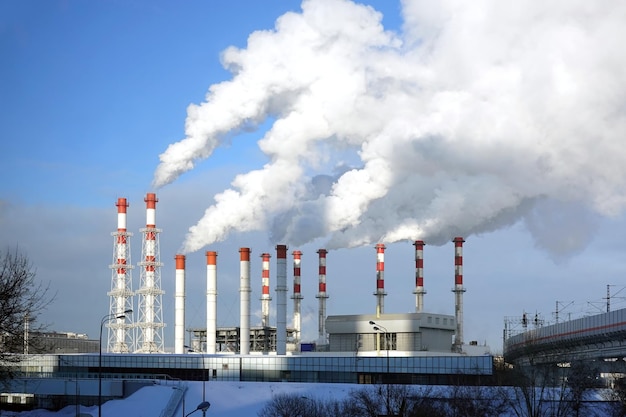 Photo bâtiment de la centrale thermoélectrique avec de nombreux tuyaux industriels rouges et blancs avec une fumée dense