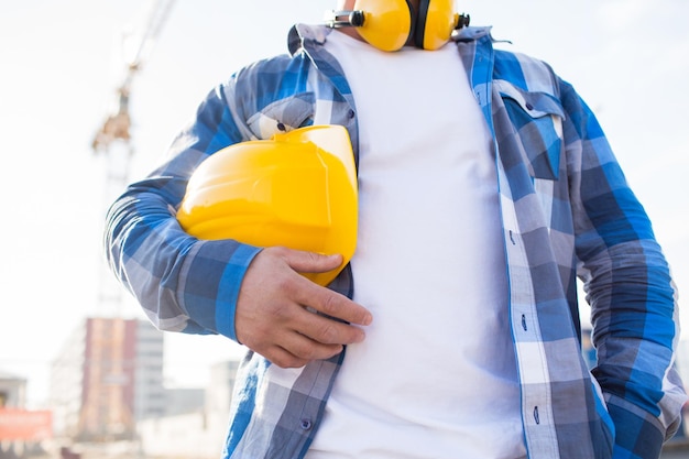 bâtiment, équipement de protection et concept de personnes - gros plan sur un constructeur tenant un casque ou un casque jaune à l'extérieur sur un chantier de construction