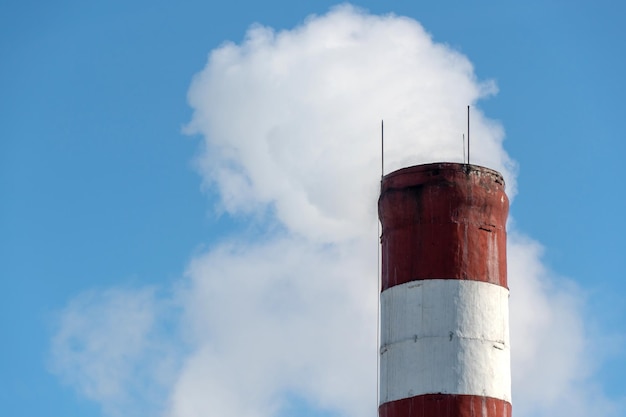 Un bâtiment industriel et une cheminée avec de la fumée blanche contre un ciel bleu Pollution de l'air par la fumée d'une usine en activité Industrie chimique et risque de catastrophe environnementale