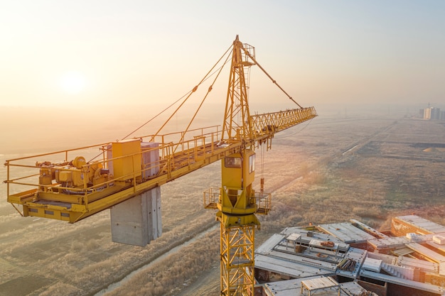 Bâtiment à plusieurs étages, grue à tour et chantier de construction, vue de dessus. Au coucher du soleil.