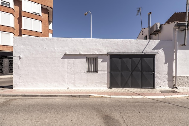 Un bâtiment urbain blanc d'un étage avec un portail gris à une intersection de rue avec des trottoirs étroits