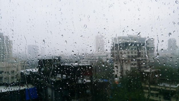 Des bâtiments vus à travers une fenêtre humide pendant la saison des pluies