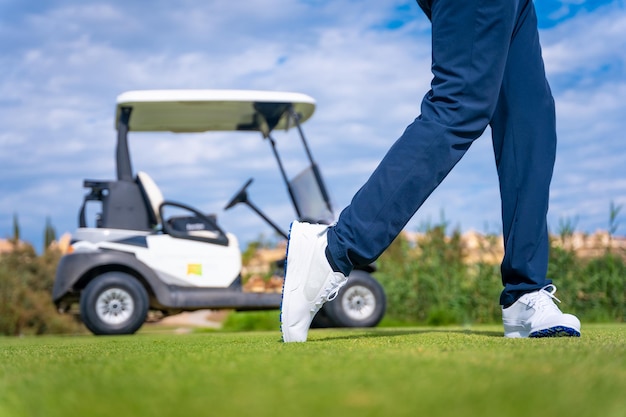 Bâton de conducteur de golf se préparant à frapper la balle Homme méconnaissable jouant au golf à côté d'une voiture buggy