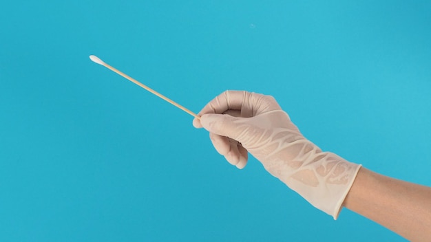 Bâton de coton pour test d'écouvillon à la main avec des gants médicaux blancs ou un gant en latex sur fond bleu.