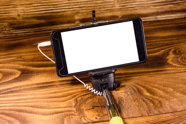 Bâton de selfie avec le smartphone moderne sur la table en bois rustique