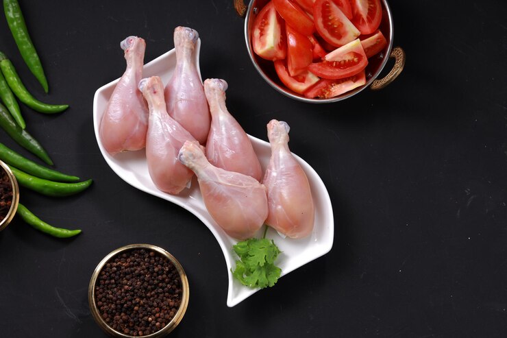 Photo bâton de tambour de poulet cru ou morceaux de jambe disposés sur de la vaisselle blanche avec un fond gris.