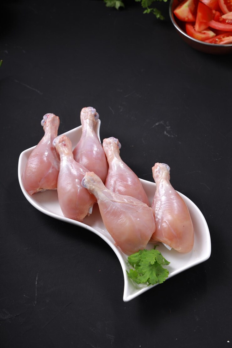 Photo bâton de tambour de poulet cru ou morceaux de jambe disposés sur de la vaisselle blanche avec un fond gris