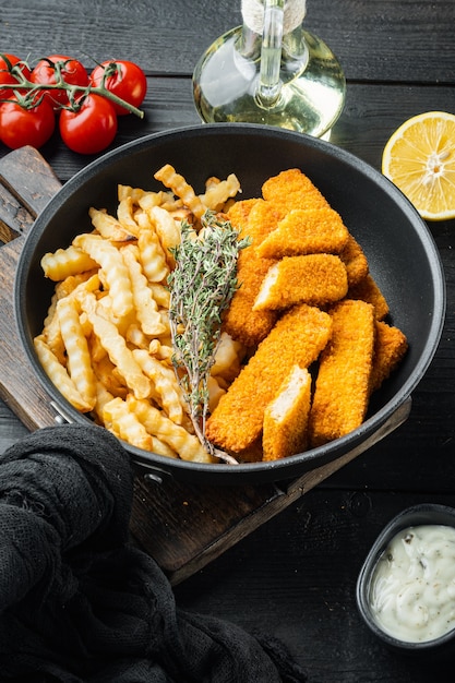 Bâtonnet de poisson frit ou poisson frites avec sauce, sur poêle en fer à frire, sur table en bois noir