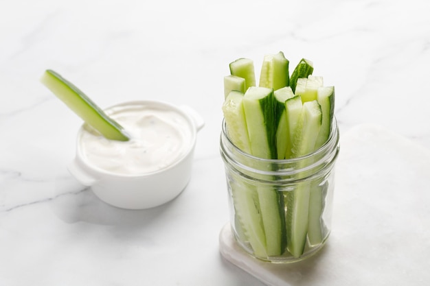 Bâtonnets de concombre dans un bocal en verre avec sauce Des collations saines Fond de marbre