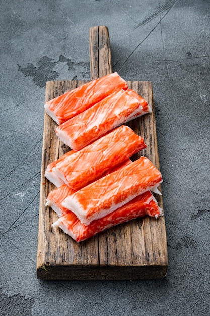 Bâtonnets de crabe aux fruits de mer hachis de poisson semi-fini avec un ensemble de crabe bleu nageant, sur une planche à découper en bois, sur fond gris