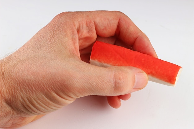 Bâtonnets de crabe à la main sur une surface blanche