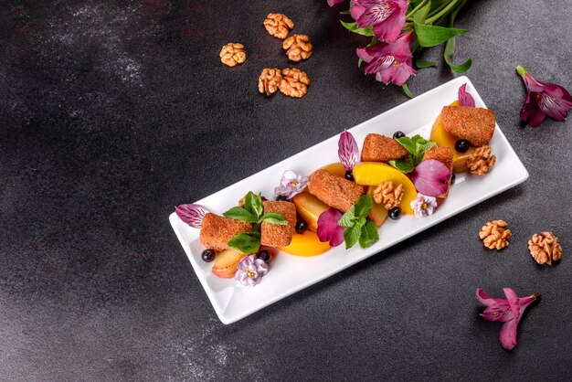 Bâtonnets de fromage parfumé frais avec pomme au four et pêche décoré de fleurs sur une plaque blanche