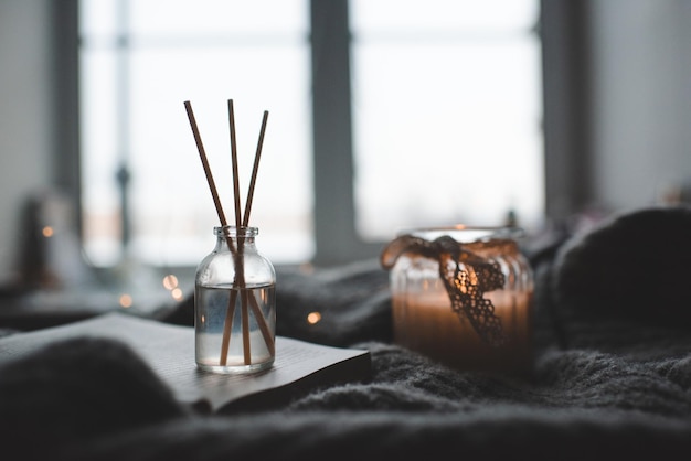 Des bâtons de bambou en bouteille avec des bougies parfumées et un livre ouvert sur un plateau en bois dans le lit en gros plan. Arôme maison. Aromathérapie.