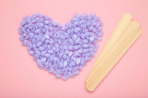 Bâtons en bois pour cire et spa avec granulés de cire en forme de coeur violet sur fond rose