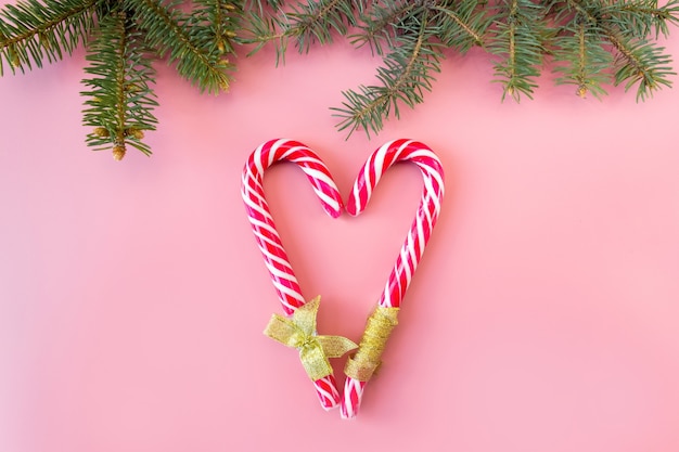 Bâtons de caramel en forme de coeur avec des branches d'épinette sur fond rose, mise à plat, vue de dessus.