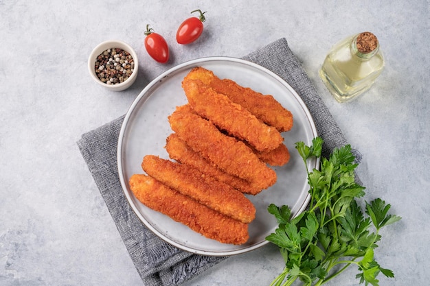 Bâtons de filet de poulet frits sur une assiette avec du persil sur un fond clair avec des tomates et des épices Nourriture diététique et saine Vue supérieure et espace de copie