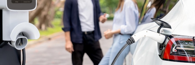 La batterie de la voiture électrique se recharge sur un fond flou d'un beau couple à l'automne Exalt