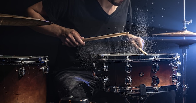 Un batteur masculin joue de la caisse claire avec des baguettes dans une pièce sombre.