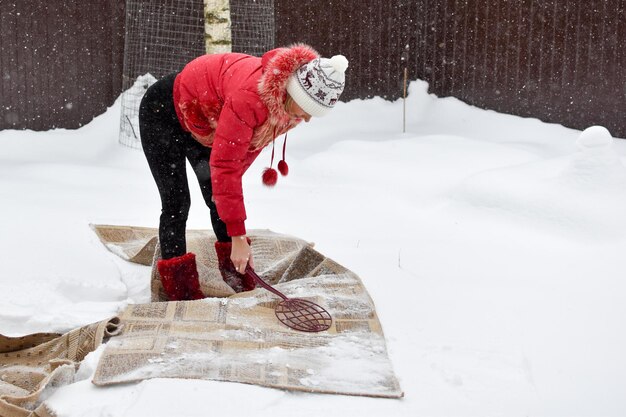 Battez le tapis de la poussière en hiver dans la neige. nettoyer les tapis de la maison avec de la neige. le tapis repose sur la neige blanche