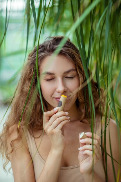 Baume à lèvres. Jolie jeune femme tenant un bâton de baume à lèvres et le sentir