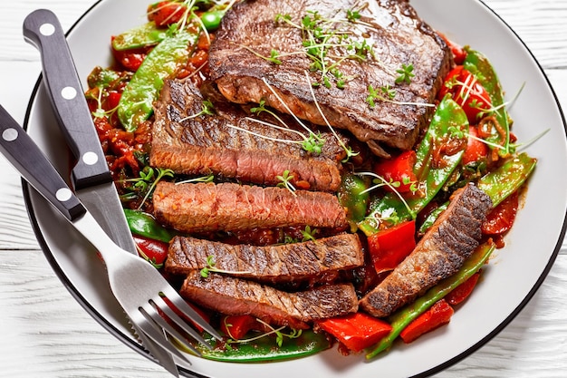 Bavette de boeuf grillée servie sur du braisé à la sauce tomate morceaux de poivron rouge mange-tout et gros plan d'oignon