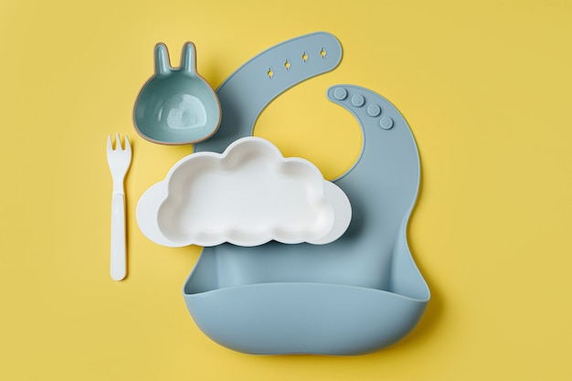 Bavoirs et assiette en forme de nuage sur fond jaune. Servir bébé. Concept de menu pour enfants, de nutrition et d'alimentation