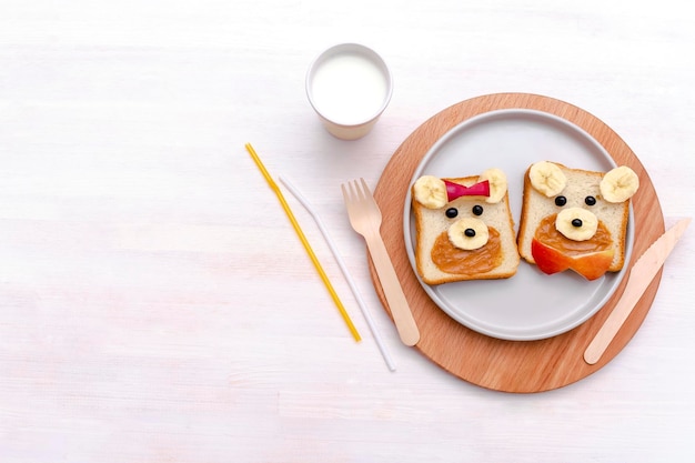 Beardog Mignon Drôle Fait Face à Un Sandwich Au Pain Grillé Avec Du Beurre D'arachide, Du Lait De Pomme à La Banane, Un Dessert Sucré Pour Enfants, Un Petit-déjeuner Sain, Un Déjeuner, De L'art Alimentaire Sur Une Assiette, Un Fond Blanc, Une Vue Rapprochée