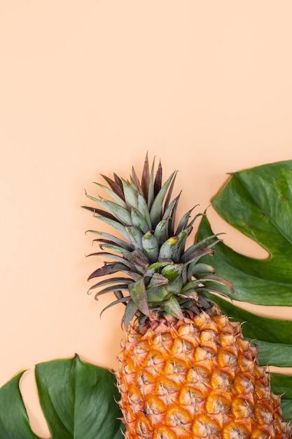 Beau ananas sur feuilles de palmier tropical monstera isolé sur fond jaune orange pastel clair vue de dessus plat posé au-dessus des fruits d'été