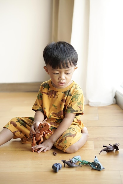 Beau bambin asiatique jouant joyeusement avec un jouet de dinosaure en plastique près de la fenêtre dans un hôtel