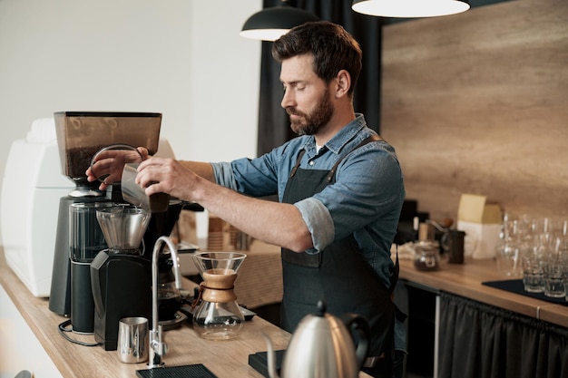 Un beau barista broie des grains de café dans une machine à café