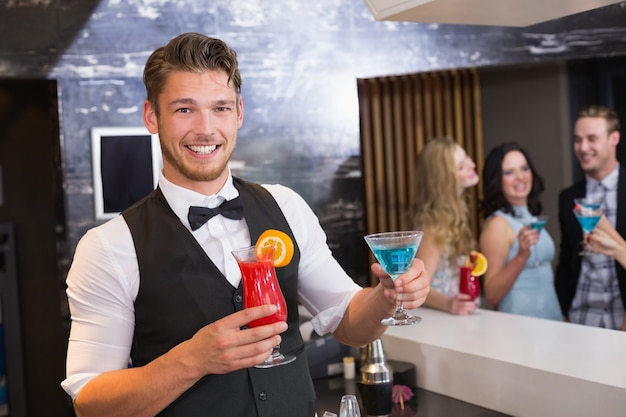 Beau barman souriant à la caméra tenant des cocktails