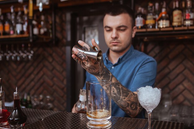 Beau barman tatoué mâle prépare un verre