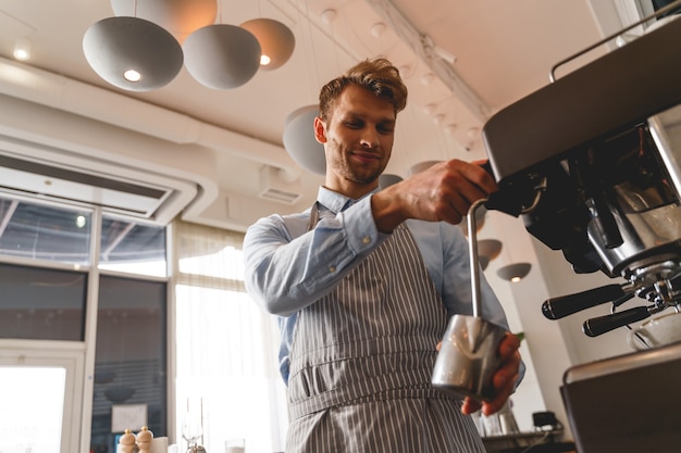 Beau barman versant une boisson chaude dans une tasse métallique du robinet de la machine à café