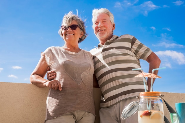 beau beau couple adulte mature de race blanche sourit et profite d'activités de loisirs en plein air ensemble sur la terrasse à la maison. boisson aux fruits de style vacances avec parapluie sur la table. concept de bonheur pour reti