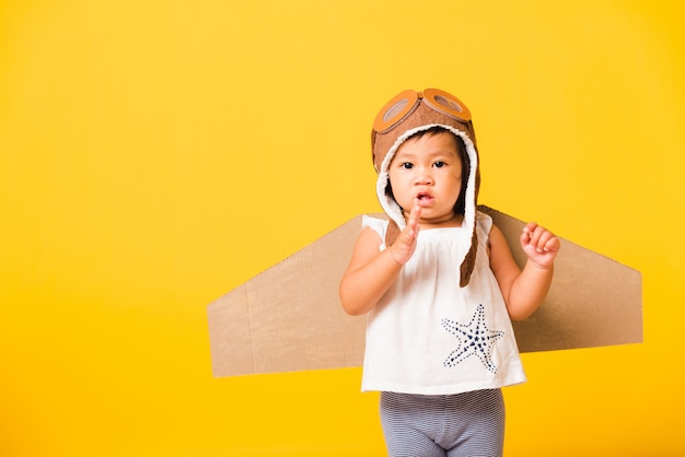 Beau bébé asiatique petite fille porter un chapeau de pilote jouant avec des ailes d'avion en carton jouet volant