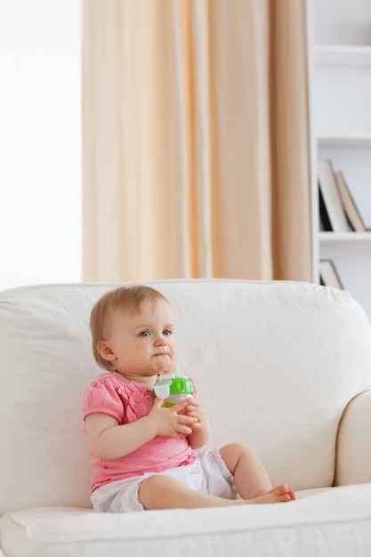 Beau bébé blond jouant avec une balle tout en étant assis sur un canapé