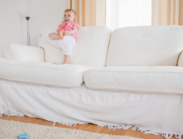 Beau bébé blond jouant avec des pièces de puzzle en se tenant debout sur un canapé