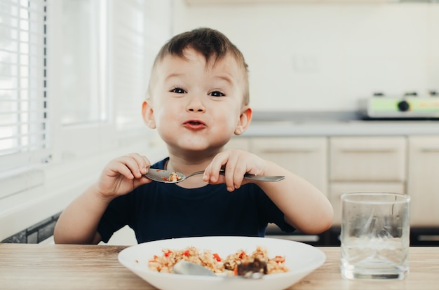 Beau bébé mignon mange du riz avec une cuillère dans la cuisine