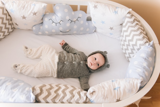 Beau bébé nouveau-né allongé dans un lit ovale avec de beaux pare-chocs dans des tons délicats de gris, bleu et blanc