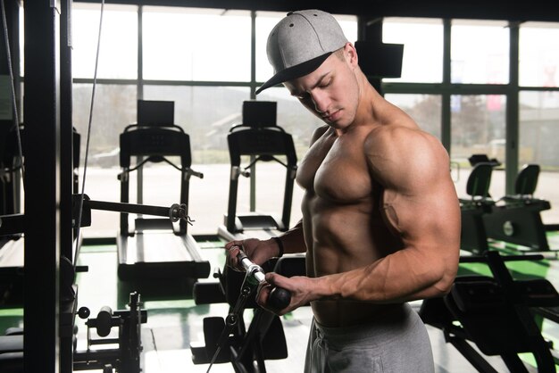 Beau bodybuilder de remise en forme musculaire faisant des exercices de poids lourds pour les biceps sur la machine avec câble dans la salle de gym